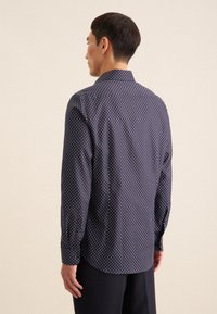 Camicia blu navy con pois bianchi. Maniche lunghe, colletto a bottoni e orlo curvo. Tessuto liscio, leggero e vestibilità classica.