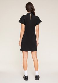 Schwarzes kurzes Kleid mit einem Schlüssellochausschnitt hinten, weit auslaufenden Ärmeln und einer strukturierten Passform. Hergestellt aus glattem Stoff mit einfachen Nähdetails.