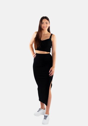 Czarny prążkowany crop top na cienkich ramiączkach, w połączeniu z czarną midi spódnicą z bocznym rozcięciem. Uzupełniony białymi trampkami.