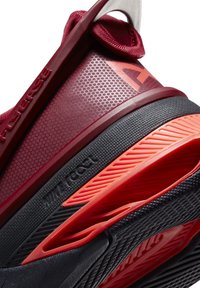 Gros plan sur le talon d'une chaussure de sport bordeaux et noire avec des motifs en relief, une semelle coussinée et des accents rouges, y compris des détails de marque.