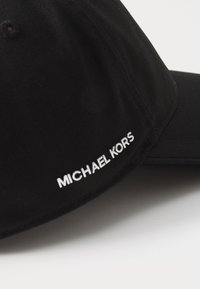 Černá kšiltovka vyrobená z látky, s ohnutým kšiltem a vyšívaným logem "MICHAEL KORS" v bílé barvě na boku.