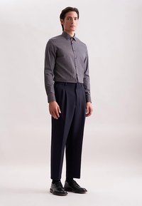 Overhemd met knopen in een donker patroon met kleine witte stippen, gecombineerd met op maat gemaakte marineblauwe broek en glanzende zwarte schoenen. Gladde stofafwerking.