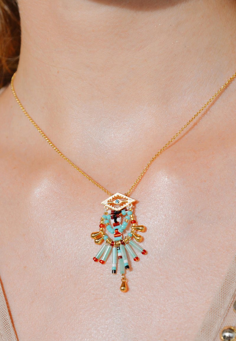 Collier en or avec un pendentif en perles de turquoise et rouges, présentant un motif d'œil et des accents de gland. Chaîne lisse avec une texture délicate.
