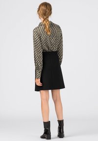 Long-sleeve, patterned blouse in beige and brown paired with a black A-line skirt, complemented by black ankle boots with a block heel.