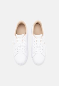 Weiße synthetische Sneakers mit minimalistischem Design, runder Zehenpartie, glatter Textur und beigen Akzenten im Innenbereich sowie im Logo.