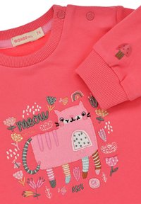 Coral sweatshirt with pink embroidered cat design. Features floral patterns, rainbow, and button accents on the shoulder. Soft texture.