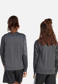 Graues, langärmliges Sporttrikot mit strukturierten gemusterten Ärmeln, aus synthetischem Material, kombiniert mit schwarzen Shorts.