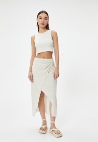 Witte geribde crop top gecombineerd met een lichtbeige wikkelrok met een zijruchette detail en een hoge split, aangevuld met chunky platform sandalen.
