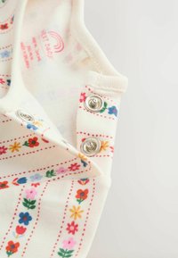 Pamut bébi rugdalózó virágmintával piros, kék és sárga színben, krémszínű háttérrel. A vállaknál patentos záródással rendelkezik.