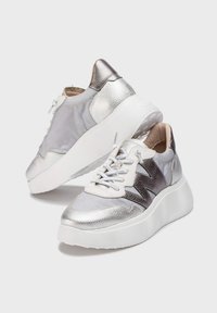 Srebrne sneakersy wykonane z mieszanki teksturowanej skórki metalicznej i gładkiego materiału, z grubą białą podeszwą i sznurowanym przodem.