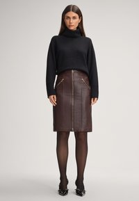 Zwarte coltrui, bruine leren kokerrok met ritsen aan de voorkant, slank ontwerp, getailleerde silhouette, gecombineerd met zwarte hakken.