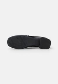 Zapato negro con parte superior de cuero liso, puntera redondeada y suela de goma texturizada que presenta un patrón para mayor tracción.
