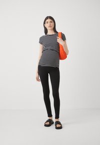 T-shirt a righe bianco e nere con maniche corte abbinato a leggings neri e sandali neri spessi. Borsa a tracolla arancione con texture tenuta a mano.