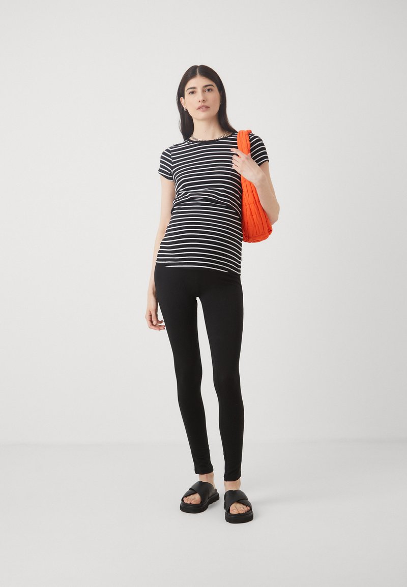 T-shirt a righe bianco e nere con maniche corte abbinato a leggings neri e sandali neri spessi. Borsa a tracolla arancione con texture tenuta a mano.
