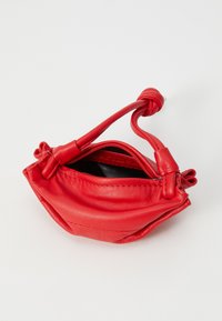 Petit sac en cuir rouge avec une anse nouée et une fermeture éclair. Il présente une texture douce et une forme arrondie avec un intérieur noir.