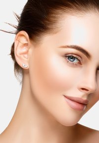 Silverfärgade stiftörhängen i hjärtform med en polerad yta. Bärs på en models örsnibb och visar en minimalistisk design.