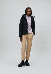 Black puffer jacket over a light purple top, beige cargo pants, and black sneakers. Notable features include zip pockets and fitted design.