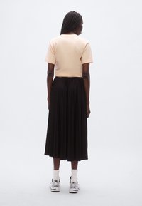 T-shirt courte pêche et jupe midi plissée noire, associées à des baskets blanches et des chaussettes courtes, vues de dos. Texture de tissu lisse.