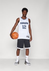 Balta krepšinio marškiniai su mėlynomis juostelėmis ir užrašu "memphis"; pilkos šortai; laiko oranžinį krepšinį; vilki juodus ir baltus batus.