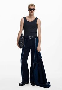 Fekete trikó és sötétkék, széles szárú nadrág fehér varrással. A modell egy fekete táskát és egy tengerészkék dzsekit tart, napszemüveget visel.