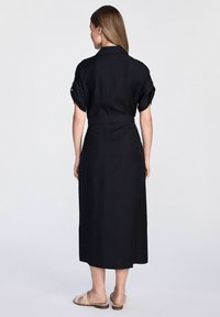 Czarna lniana sukienka koszulowa z krótkimi, podwiniętymi rękawami, z paskiem w talii i długim, prostym krojem. Gładka tekstura bez widocznych wzorów.