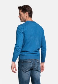 Blauwe gebreide trui met lange mouwen, ronde hals, geribde zoom, gecombineerd met middelmatige denim jeans. Gelaagd oppervlak zonder zichtbare patronen.