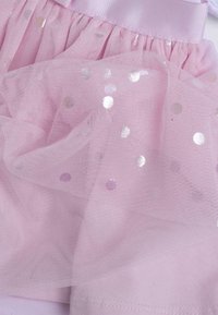 Tessuto in tulle rosa con pois iridescenti sparsi; presenta una vita arricciata e una texture morbida per un aspetto stratificato.