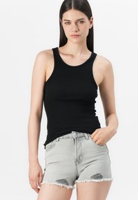 Svart ribbet tanktopp med brede stropper, kombinert med lysegrå slitte denimshorts med frynsete kanter og utskårne detaljer.