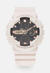 Montre G-SHOCK avec un bracelet en résine blanche, un cadran noir et doré, des affichages analogiques et numériques, et une lunette de protection. Comprend une résistance aux chocs et un calendrier.