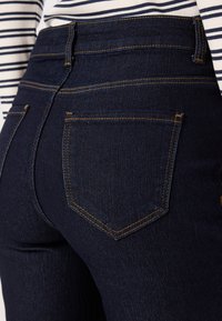 Mörkblå denimjeans med en figursydd passform. Har två bakfickor med guldtråd och en hög midja. Slät textur.