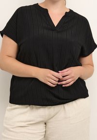 Haut noir à manches courtes avec un col en V, présentant une texture à rayures verticales. Associé à un pantalon clair, léger et ample.