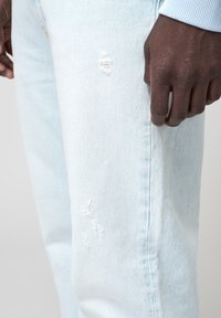 Vaaleansiniset farkut, joissa on kulutuspisteitä ja sileä pinta, slim fit -mallilla ja näkyvällä ompelulla sivusaumassa.