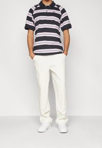 Navy- och rosa randig kortärmad pikétröja med krage, ihop med off-white byxor och vita sneakers. Enkelt design med avslappnad passform.