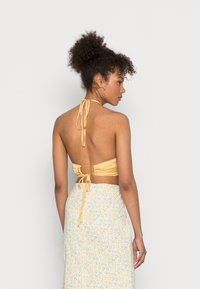Top halter amarelo claro, sem costas, com fecho de laço, feito de tecido suave; combinado com uma saia leve de padrão floral.