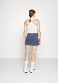 Camiseta sin mangas blanca con espalda racerback y diseño ajustado, combinada con una falda plisada azul oscuro, completada con calcetines deportivos blancos y zapatillas.