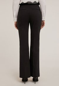 Svarta vida byxor med en slät yta, midjehögt midjeband och två bakfickor. Bärs med en vit skjorta och högklackade skor.