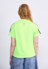 Κοντομάνικο, φωτεινό νεον πράσινο αθλητικό μπλουζάκι με μαύρες λεπτομέρειες, με στρογγυλή λαιμόκοψη και λεπτομέρεια λογότυπου στην πλάτη.