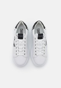 Hvite joggesko med en glatt skinnfinish, med svarte detaljer på hælen, runde snører, og "Karl Lagerfeld"-merke på tungen.