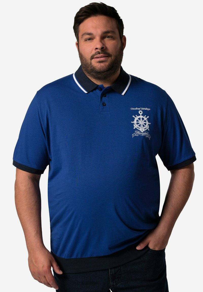 Modrá polo košile s černým límečkem a manžetami. Na hrudi má námořnický vzor s bílou výšivkou a knoflíky.