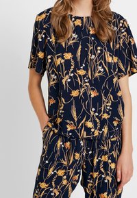 Marinblommig blus med korta ärmar som har mönster av gula och vita blommor, tillverkad av lättviktig tyg med en avslappnad passform.