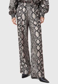 Pantalons à jambes larges en imprimé serpent noir et gris, fabriqués dans un tissu lisse avec une taille élastique et une légère brillance. Accentué par des chaussures pointues noires.