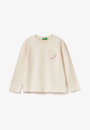 Camiseta de manga larga crema con tejido suave. Presenta dos apliques de tela con forma de rosa texturizada y texto bordado "eres genial" en el pecho.