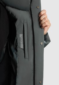 Szara pikowana kurtka z zamkiem błyskawicznym i zatrzaskiem. Wnętrze posiada kieszeń i tekstylną etykietę. Materiał wydaje się gładki i ocieplany.