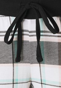 Svart dragsko på en ribbad midjeresår, i kombination med ett rutmönster i vitt, svart och pastellfärger, har en slät textur.