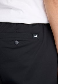 Fekete sportnadrág, sima anyagból készült, hátul gombos zsebbel és kis New Balance logós címkével.
