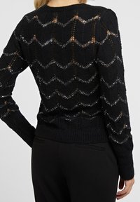 Maglione nero lavorato a maglia con motivo a onde e fili metallici, maniche a coste e orlo a coste. Tessuto testurizzato con un design a punto aperto.