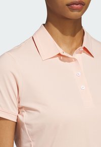 Světle růžová polo košile s klasickým límcem, zapínáním na tři knoflíky a krátkým rukávem. Vyrobena z hladkého, prodyšného materiálu.