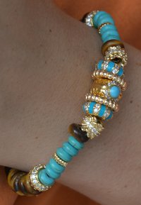 Bracelet en perles avec des accents en turquoise, des détails dorés et des strass transparents. Différentes formes de perles, y compris des styles ronds et à disque.