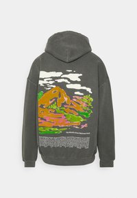 Felpa con cappuccio grigia caratterizzata da un design paesaggistico colorato sul retro, con montagne, nuvole e testo riguardante il primo parco nazionale.