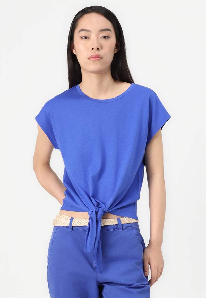 Blaues T-Shirt mit kurzen Ärmeln, aus weichem Stoff. Kombiniert mit blauen Hosen und einem gewebten beigen Gürtel, der einen lässigen, entspannten Stil präsentiert.